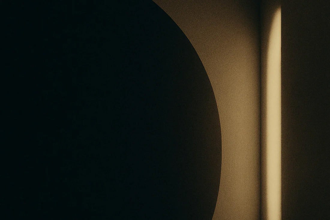 Abstrakte, minimalistische Szene mit dunkler, runder Form im Vordergrund und warmem Lichtstreifen im Hintergrund – ruhige, elegante Licht-Schatten-Komposition.