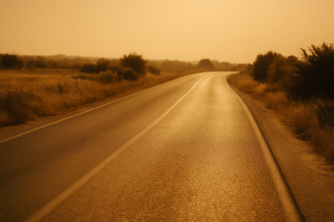 Warme, sonnengetränkte Landstraße, die in weichem Goldlicht nach Süden führt. Flirrende Hitze über dem Asphalt, helle Staubtöne in der Landschaft, ruhige weite Stimmung.