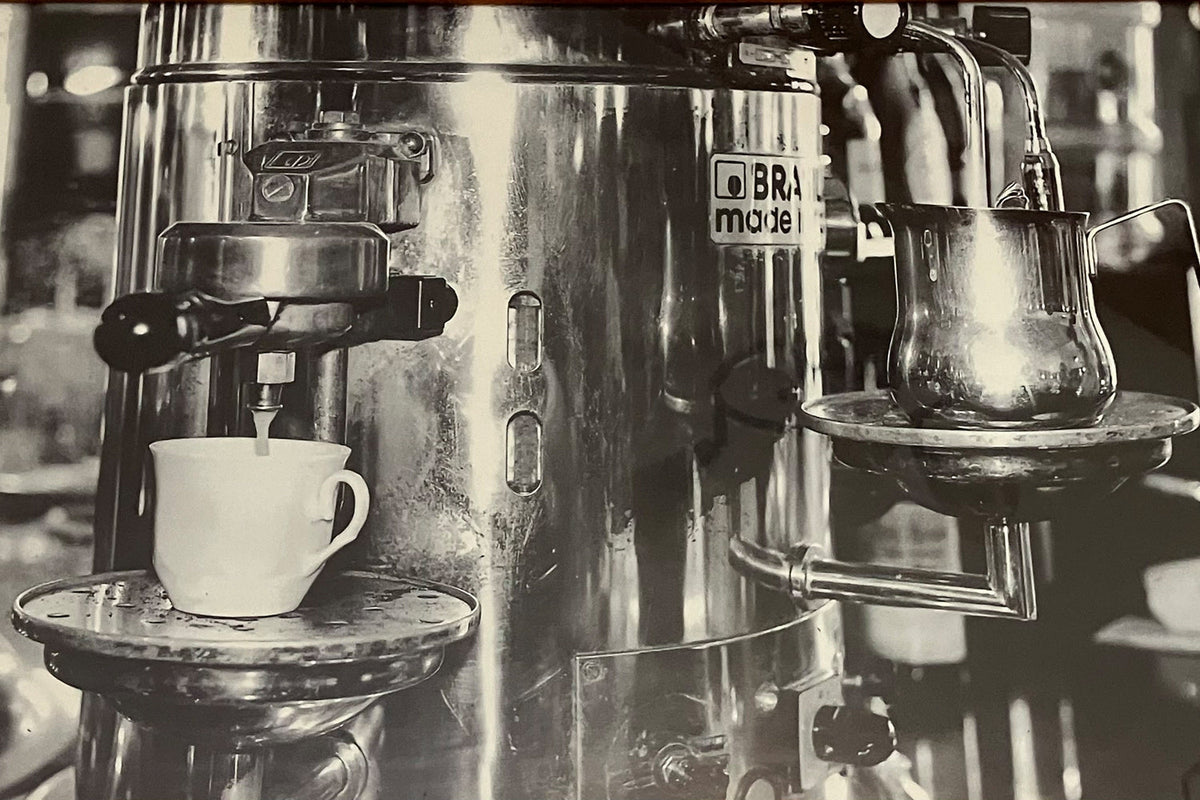 Schwarz-weiß Aufnahme einer klassischen Brasilia Espressomaschine in einem italienischen Café, glänzender Siebträger und Tasse darunter.