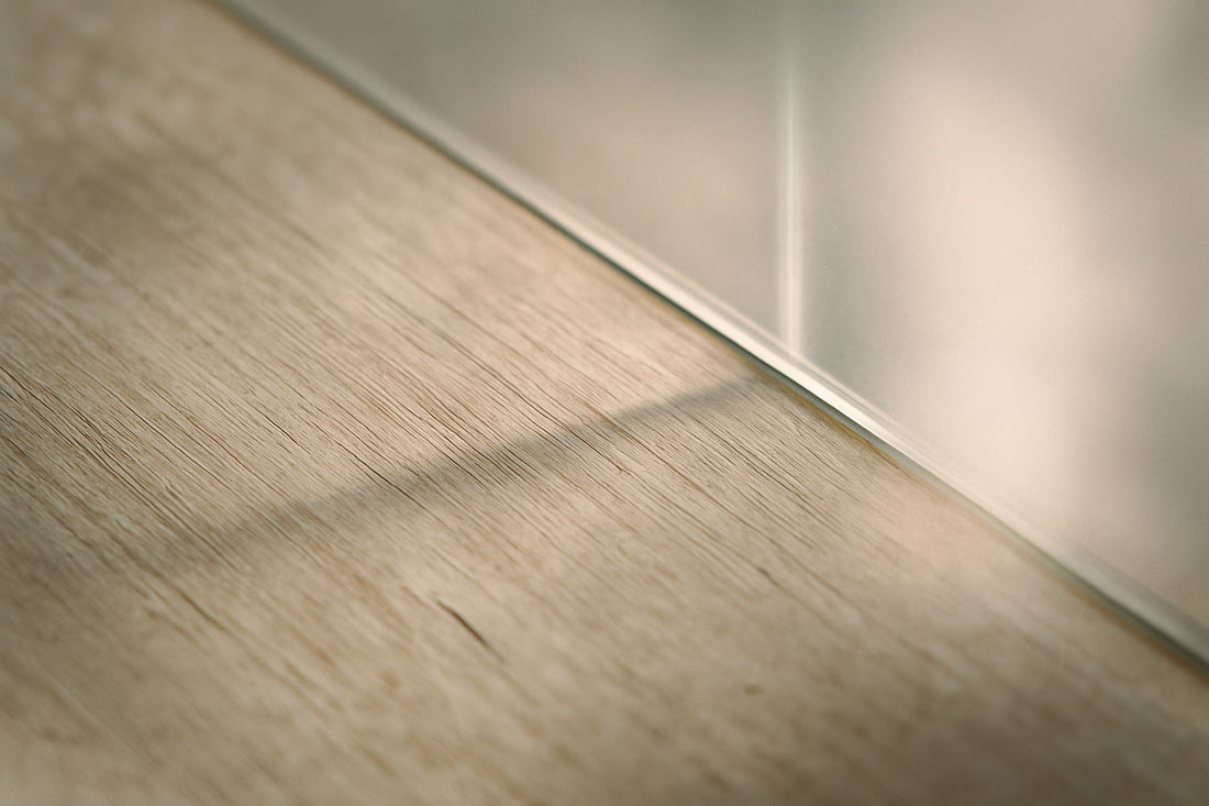 Detailaufnahme einer Holzfläche mit einer Glaswand im sanften Seitenlicht – feine Maserungen, Lichtreflexe und weiche Schatten erzeugen ein stilles, poetisches Spiel aus Material, Zeit und Resonanz.
