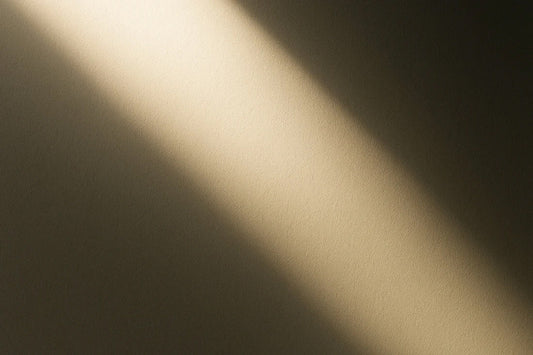 Weicher Lichtstreifen fällt diagonal durch einen dunklen Raum und erzeugt eine stille, abstrakte Licht-Schatten-Atmosphäre.