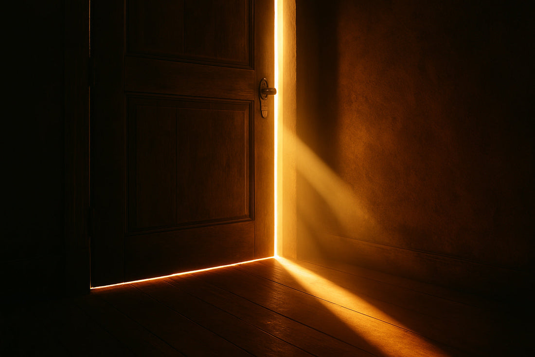 Ein schmaler Streifen warmen Lichts fällt durch einen Türspalt in einen dunklen Raum und zeichnet eine klare, minimalistische Linie aus Licht und Schatten