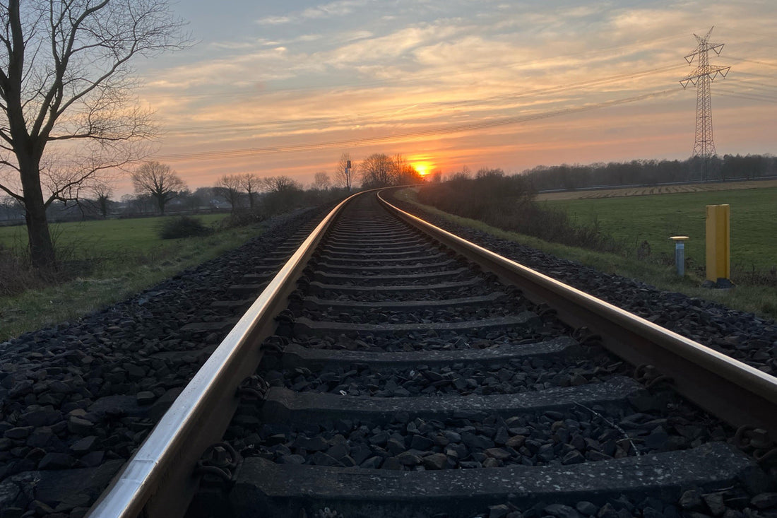 Zwei Eisenbahngleise im warmen Abendlicht, verlaufen ruhig in die Ferne. Das Licht spiegelt sich auf dem Stahl, umgeben von stiller Landschaft – ein Sinnbild für Richtung, Reise und die leise Klarheit des Unterwegsseins.