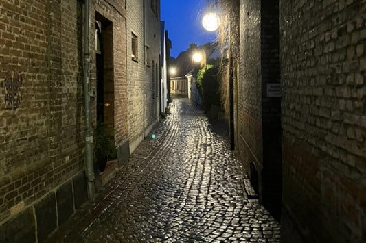 Schmale alte Gasse mit glänzendem Kopfsteinpflaster und warmen Laternen, Abendhimmel im Hintergrund. Ruhige, zeitvolle Stimmung zwischen Licht und Geschichte