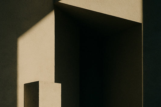 Ein minimalistisches, architektonisches Schatten-Licht-Motiv: harte Sonnenstrahlen schneiden diagonale Formen in eine beige Wand, während ein senkrechter Pfeiler und ein tiefes Rechteck im Schatten stehen.