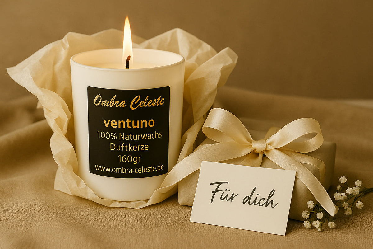 Elegante Ombra Celeste Duftkerze ventuno in Geschenkverpackung, brennend mit goldener Flamme, daneben Karte Dür dich, Satinband und weißen Blüten - stilvolles Geschenk mit Bedeutung.