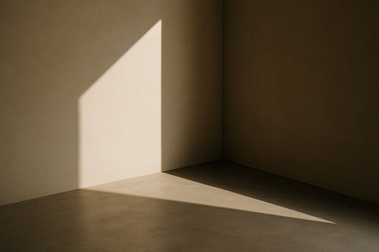 Minimalistische Raumecke in warmem Licht; diagonaler Lichtkeil fällt präzise auf Boden und Wand, klare Schattenkante, ruhige architektonische Atmosphäre im High-Fashion-Stil.