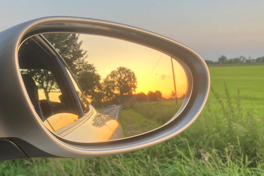 Rückspiegel im warmen Abendlicht mit Blick auf eine ruhige Landstraße, weiche Farben, friedliche Stimmung zwischen Weg und Licht