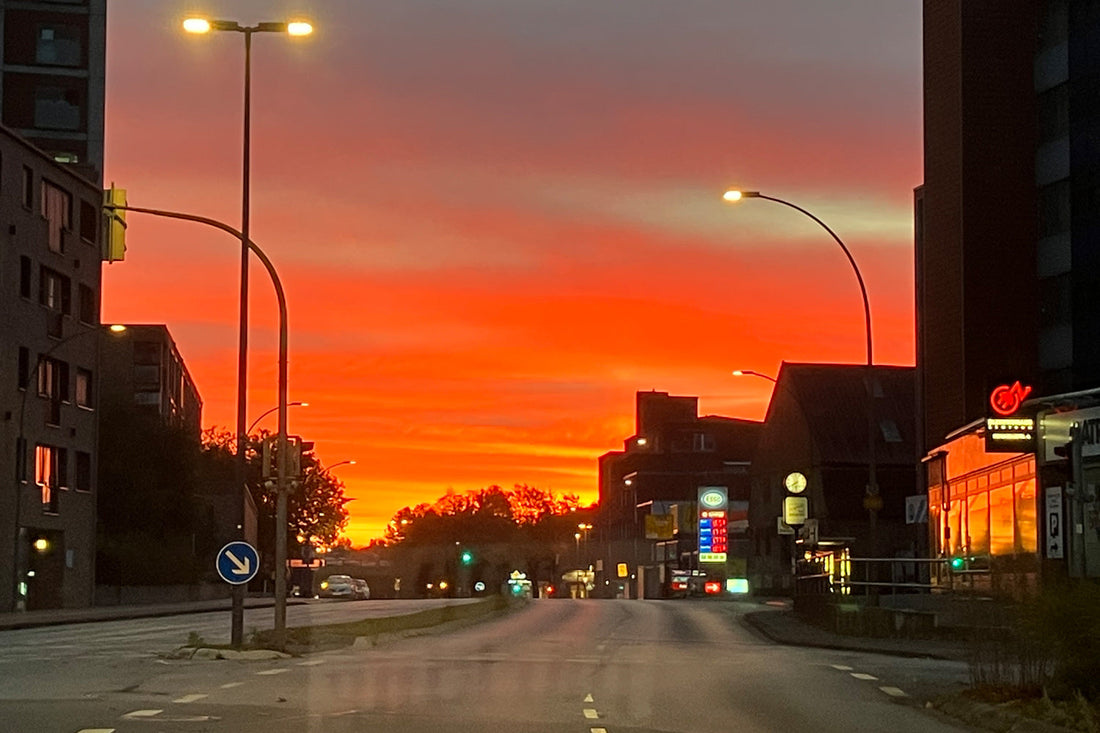 Früher Morgen auf leerer Straße, roter Himmel spiegelt sich in der Windschutzscheibe eines Lancia – ein stiller Moment zwischen Nacht und Leben.