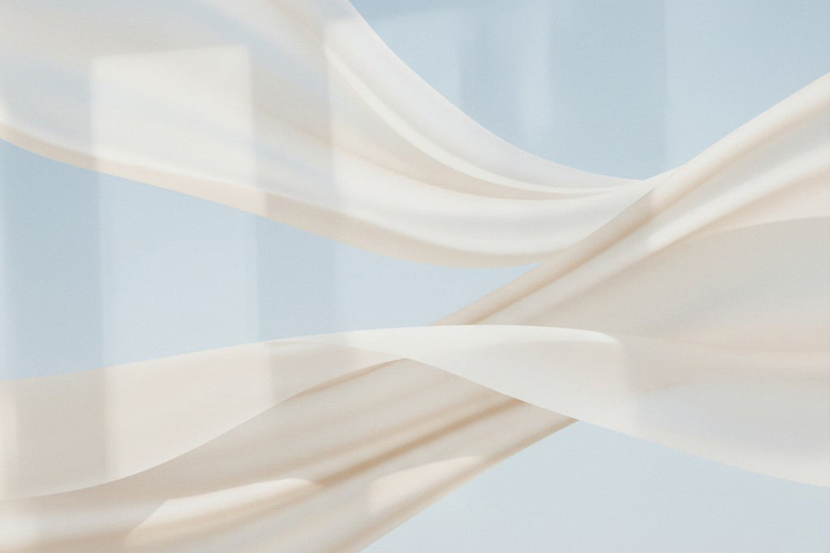 Sanftes, helles Tuch bewegt sich in weichen Wellen vor einem zarten blauen Hintergrund – Licht und Stoff verschmelzen zu einer ruhigen, luftigen Komposition, die Leichtigkeit und Offenheit ausstrahlt