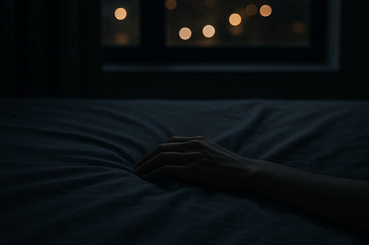Eine Hand liegt auf einem Bettlaken, im Hintergrund unscharfe Stadtlichter durch ein Fenster – stille, urbane Szene über Träume und das innere Erleben der Nacht