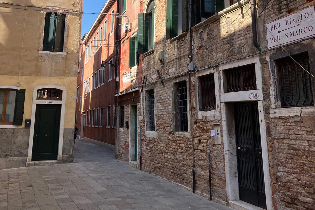 Schmale venezianische Gasse mit alten Fassaden, verwittertem Mauerwerk und offenstehenden grünen Fensterläden im warmen Tageslicht