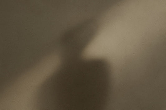 Diagonal, weicher Schatten auf einer warmgrauen, leicht strukturierten Wandfläche; abstrakte, stille Komposition im modernen Ombra-Celeste-Editorialstil.